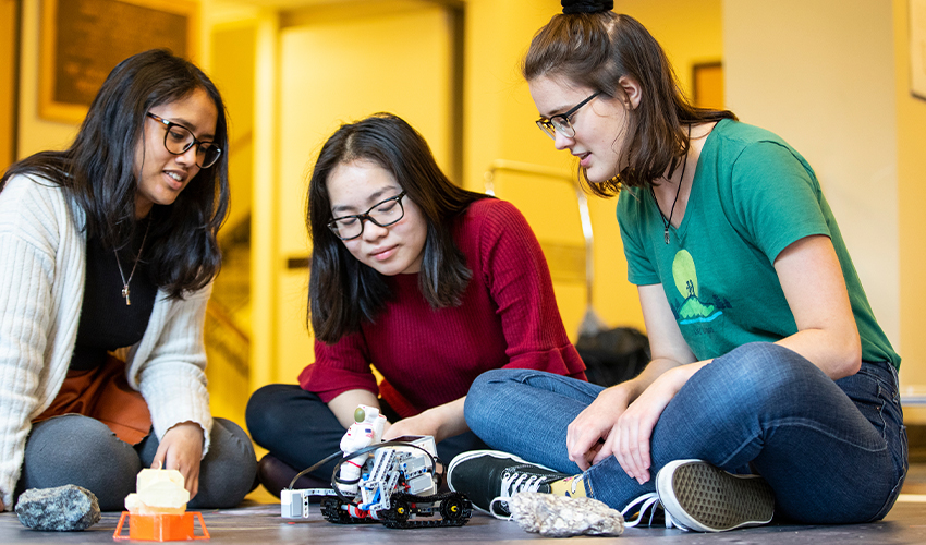 Three women looking at a small robot prototype