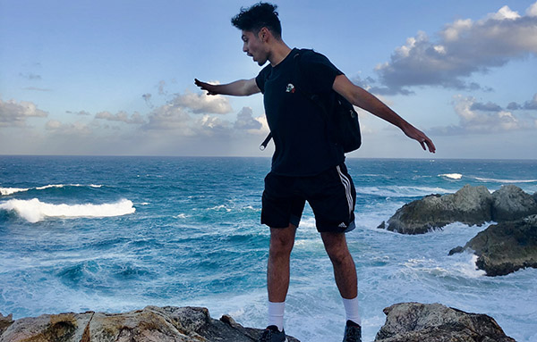 a young man standing on a rock with water behind him