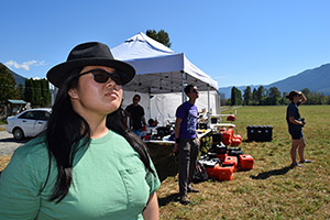 three students outside a tent staring at the sky at recently launched UAV