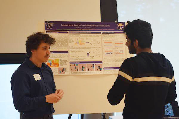 Isaac Remy standing next to his research poster and listening to a person talking