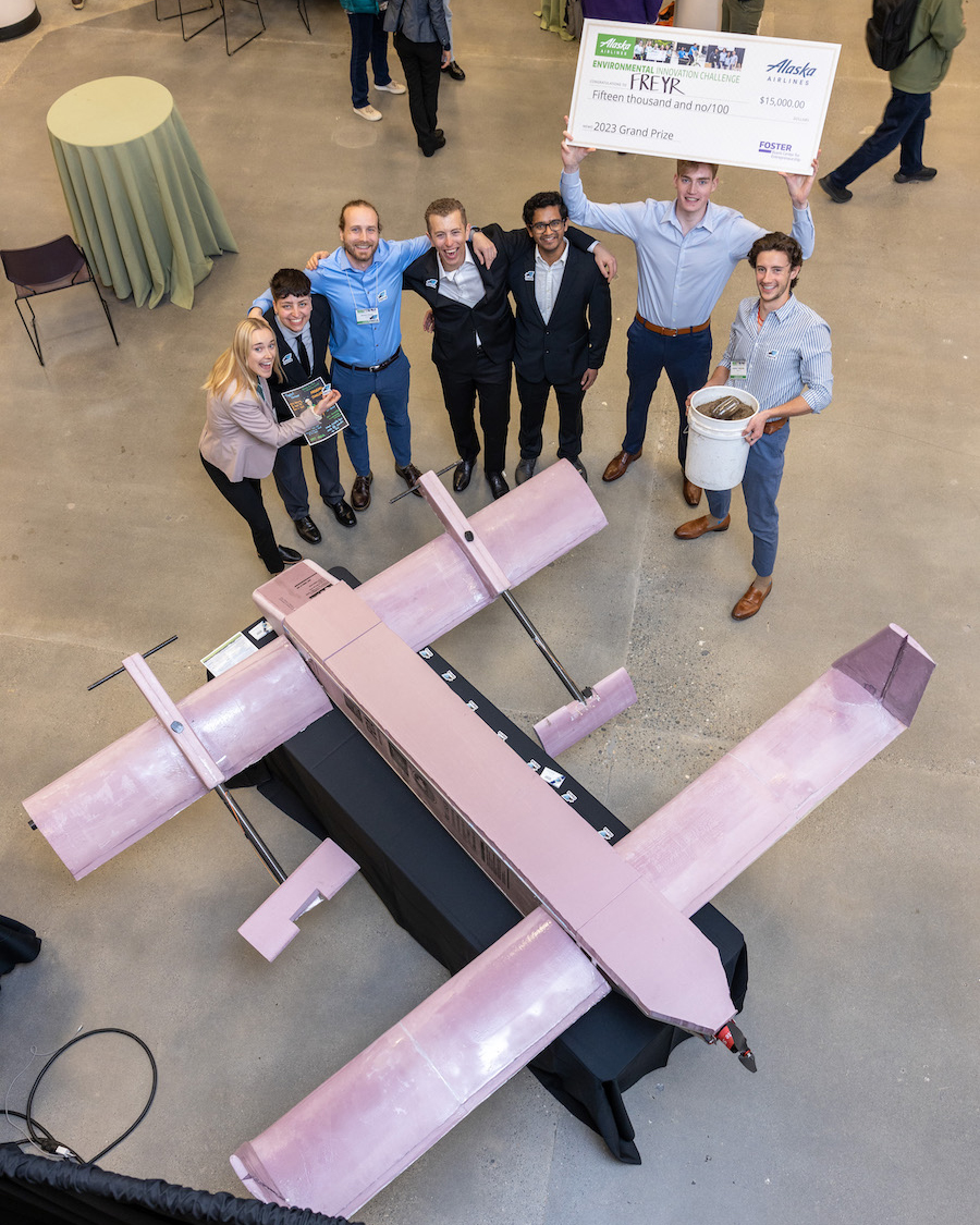 Prize team winners and one holding a big check next to a plane prototype