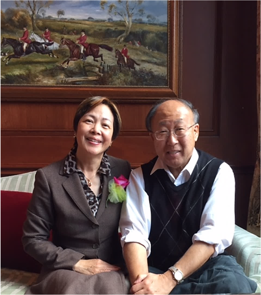 Catherine and Mike Taniguchi sitting in a couch and smiling to the camera