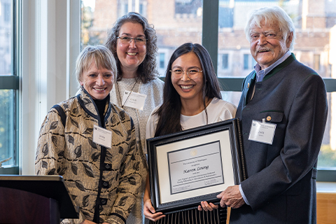 A person is holding an award frame, surrounded by three other people.