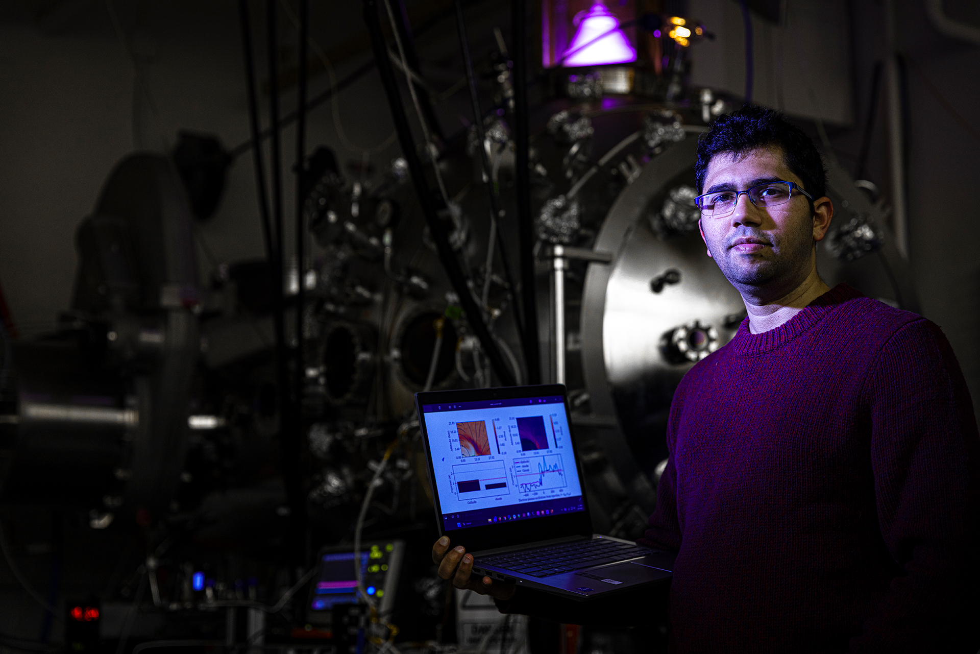 Arvindh Sharma in a laboratory holding an open laptop, surrounded by scientific equipment