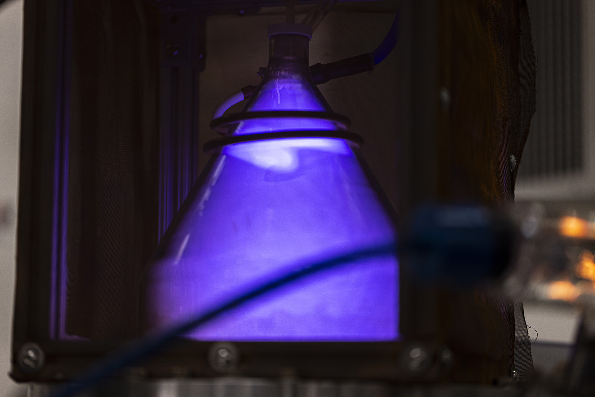 Glowing violet plasma within a conical glass structure inside a metallic frame
