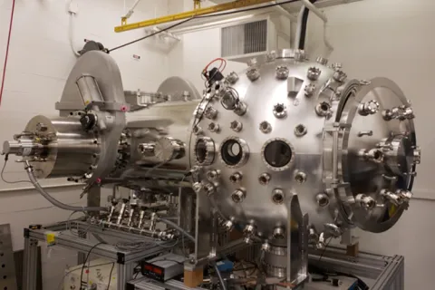 A large metallic cylindrical and spherical laboratory machine with numerous ports and cables.