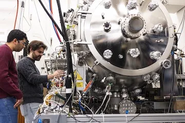 Two students with large metal equipment.